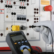 Technician measuring voltage on an electric vehicle training panel using a digital multimeter and insulated gloves